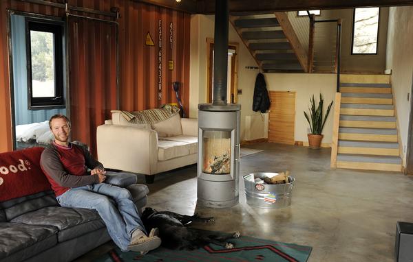 Andrew McMullin sits in his living room with his dog around the fire place at his home in Nederland, Colorado, which was built with with shipping containers on Tuesday, December 4, 2012. One can see the container ID numbers on the wall in the background. Cyrus McCrimmon, The Denver Post